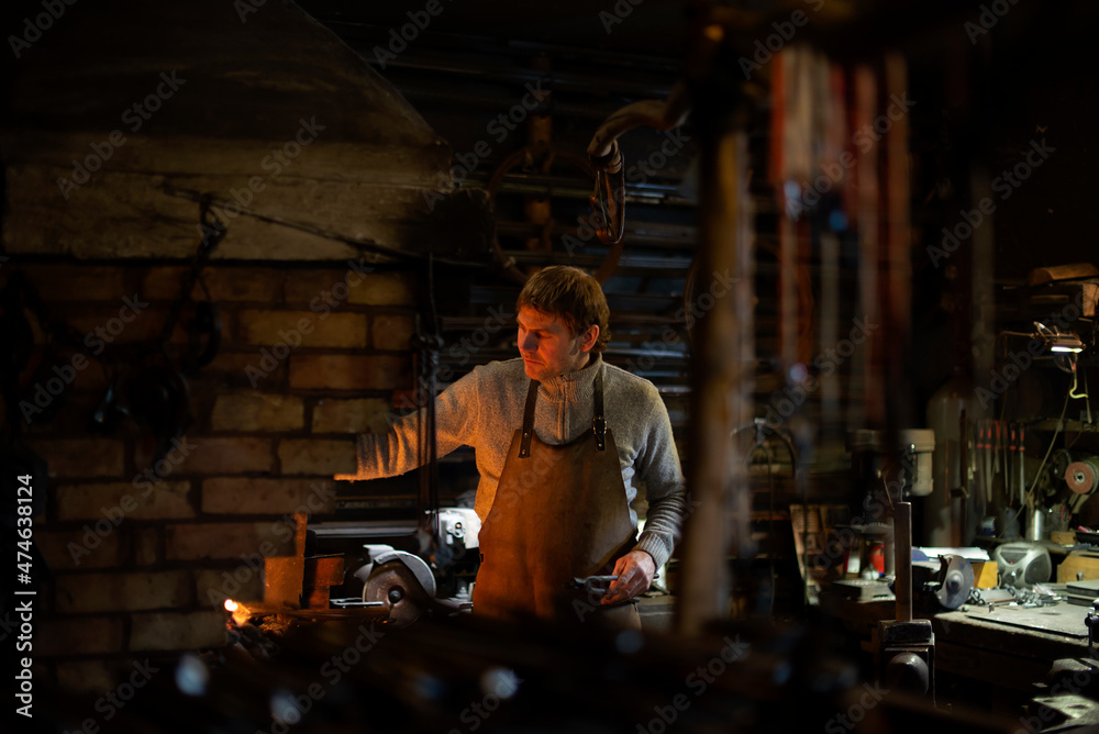 Obraz premium Latvian blacksmith working with open fire in furnace. The blacksmith forging hot iron in workshop