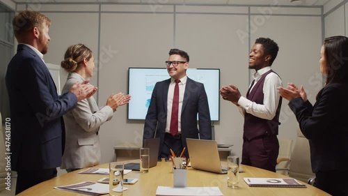 Dolly-out shot of happy male executive delivering news of successful year of company to team of businesspeople, then smiling as they are applauding