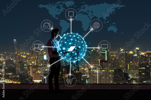 Asian businessman standing and using the laptop for online shopping with omni channel over the cityscape background at night time, Business success and technology concept photo