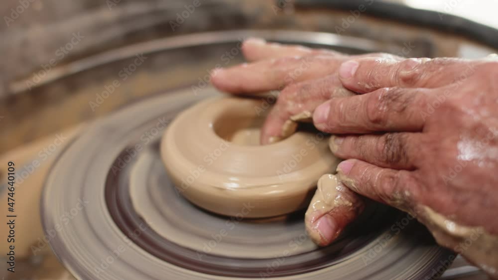 Professional potter turns wet clay on potter's wheel and gives it shape with recess with his fingers. Macro. Concept of making dishes from clay Professional potter turns wet clay on potter's wheel and gives it shape with recess with his fingers. Macro. Concept of making dishes from clay
