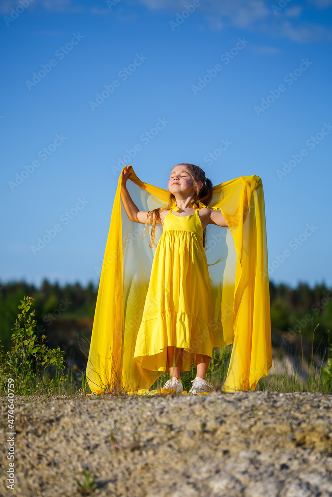 Beautiful blonde girl posing in a yellow dress in nature. Summer photo. Blue sky. Sunny day.