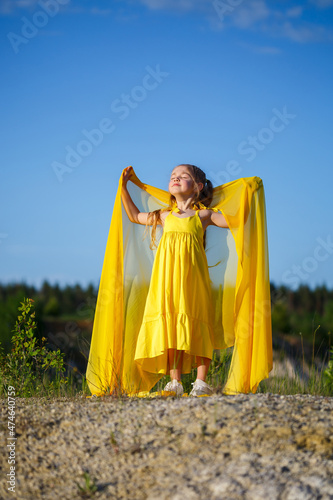 Beautiful blonde girl posing in a yellow dress in nature. Summer photo. Blue sky. Sunny day.