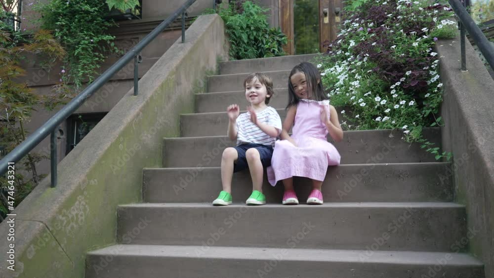 View of a little boy and a little girl sitting on brownstone stoop ...
