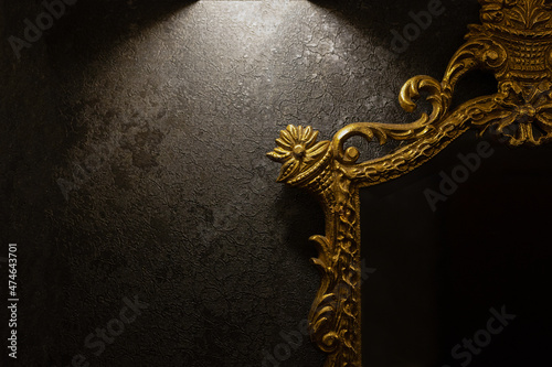 A vintage mirror with a golden frame hung on a dark wall