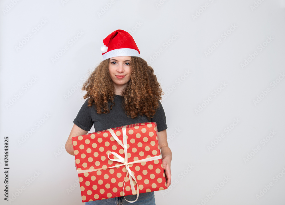 Happy excited young woman in santa claus hat with curly hair and gift box over white background Happy excited young woman in santa claus hat with curly hair and gift box over white background