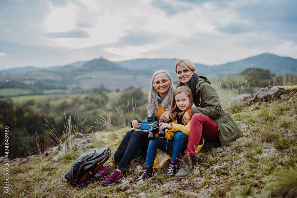 Small girl with mother and grandmother sitting and lookiong at camera on top of mountain.