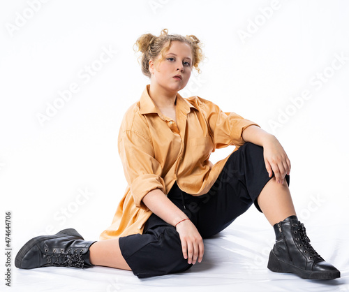 girl in black pants and a shirt sits on the floor in the studio. model posing for the camera. model pose. isolated, white background