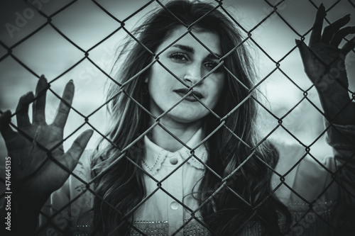 the girl looks at the camera through the net. look through the fence. black and white photography. model on the other side of the fence. out of focus.