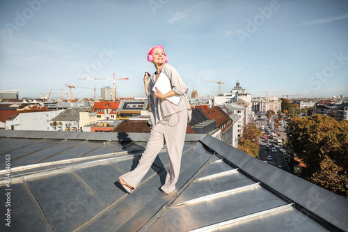 Woman with laptop and headphones standing on rooftop photo