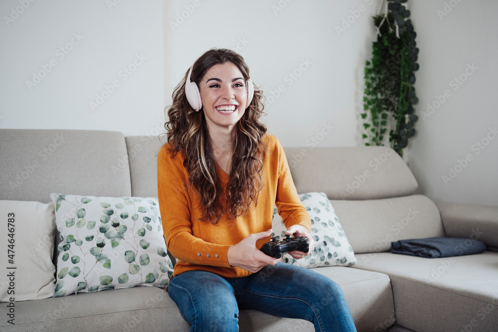 © Westend61 - Happy woman with headphones playing game through joystick at home