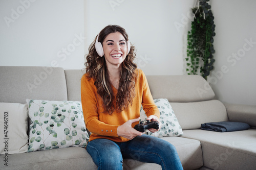 Happy woman with headphones playing game through joystick at home