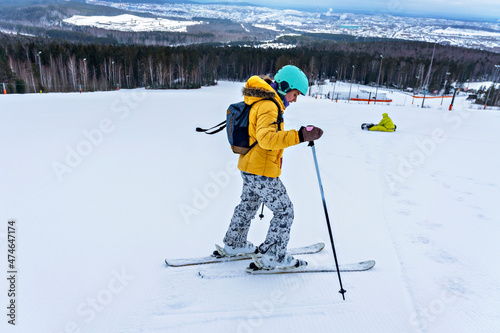 Young woman in yellow jacket and ski helmet skiing down on mountain slope, winter sports, alpine skiing outdoors activity, healthy lifestyle