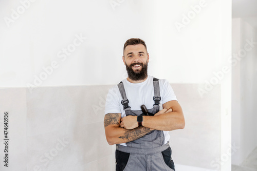 A hardworking, successful bearded painter is standing proudly with arms crossed in the freshly painted room. He did a good job. It is very important to have an experienced worker.
