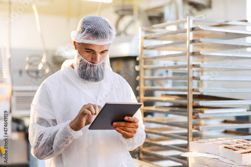 A supervisor in a sterile uniform is standing in a food factory and using his tablet to check on productivity. photo