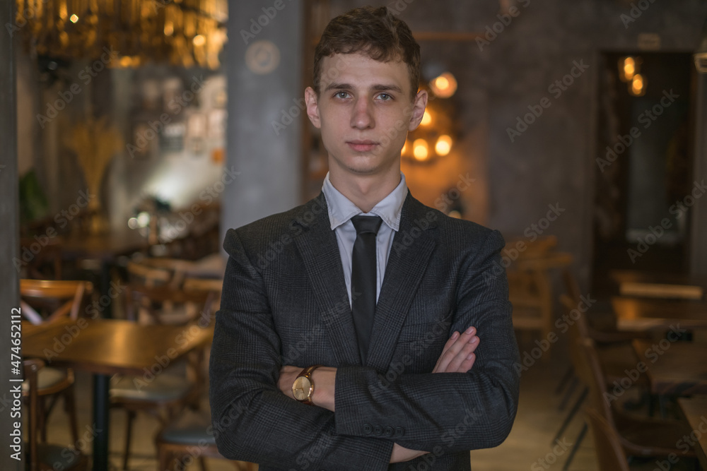 Portrait of young caucasian business man in formal suit standing in the bar with crossed arms. Handsome man standing in the coffee shop Portrait of young caucasian business man in formal suit standing in the bar with crossed arms. Handsome man standing in the coffee shop