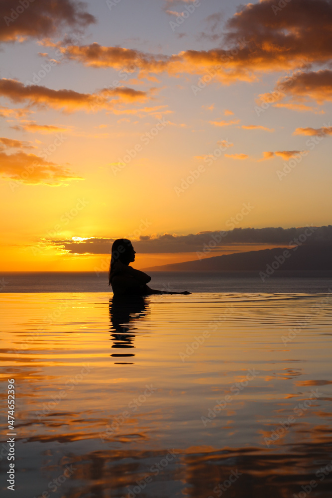 TENERIFE . SPAIN. the Girl put her hand on her shoulder and stands in the pool, against the background of an orange sunset and the ocean. 