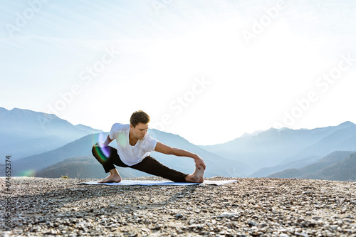 Flexible man practicing Skandasana with mountain view photo