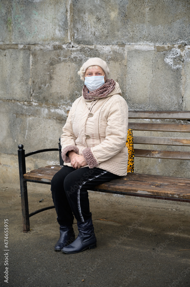 Aged woman at bus stop wearing face mask during coronavirus outbreak.