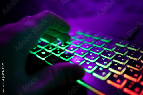 Hands on a glowing keyboard on a colored abstract background. The gamer plays the keyboard. Close-up.