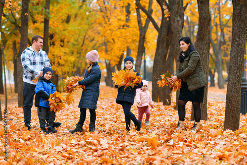 Portrait of a family with children in an autumn city park - happy people walking together, they toss the leaves, beautiful nature with yellow leaves as background. © soleg