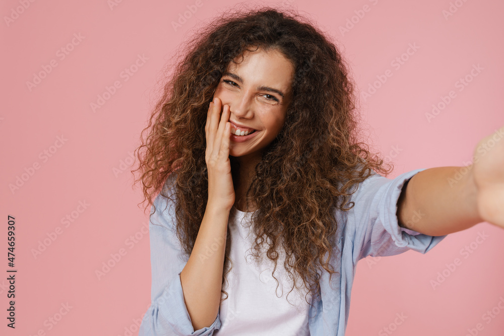 Young brunette woman with wavy hair smiling while taking selfie photo