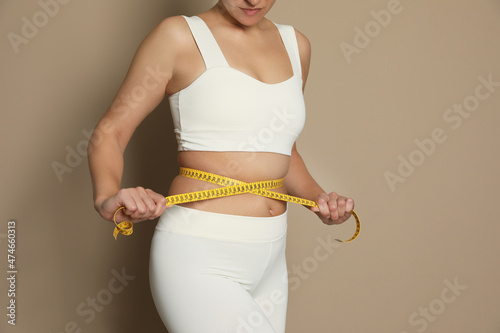 Woman measuring waist with tape on beige background, closeup © New Africa