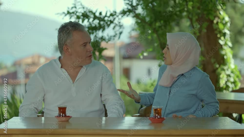 Muslim woman in hijab and her husband are drinking tea in a cafe.A family that fights and has problems in their marriage.The man raises his hand to hit his wife.The concept of violence against women.