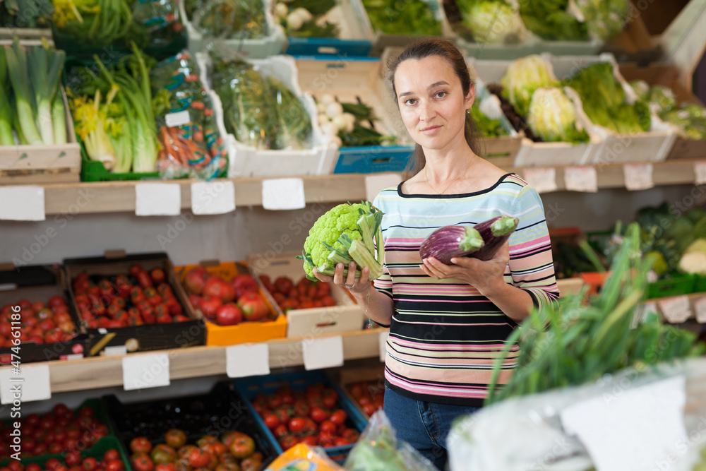 Positive Caucasian female choosing fresh broccoli at supermarket