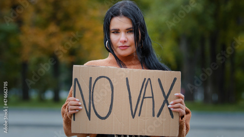 Young confident hispanic woman holding cardboard sign no vax protesting against vaccination outdoors serious girl standing on street demonstrates protest immunization covid19 stop untried vaccine