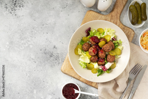Swedish meatballs with salad, pickled cucumber and lingonberry jam in a bowl. A traditional Scandinavian dish in a ceramic plate on a light gray culinary background. Top view with a copyspace