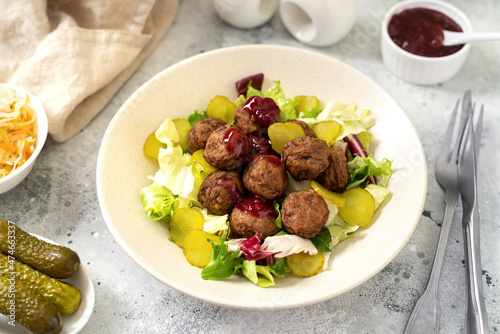 Swedish meatballs with salad, pickled cucumber and lingonberry jam in a bowl. Traditional Scandinavian dish in a ceramic plate on a light gray culinary background closeup