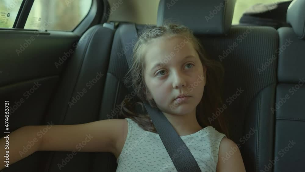 Little girl traveling in the back seat of the car looking out the car ...