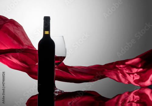 Вottle and glass of red wine on a reflective background.