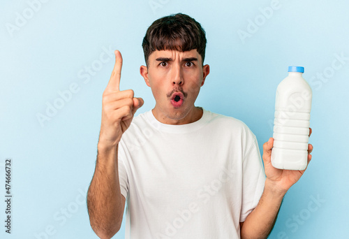 Young mixed race man holding a bottle of milk isolated on blue background having an idea, inspiration concept.