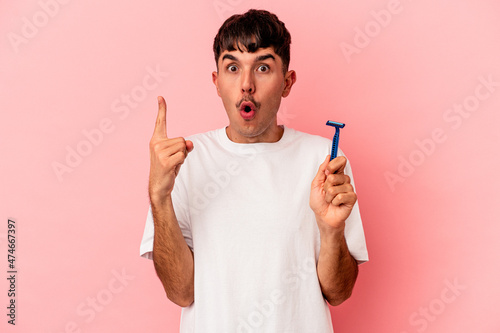 Young mixed race man holding razor blade isolated on pink background having some great idea, concept of creativity.