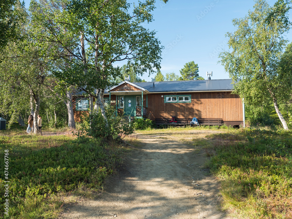 Frontal view of one of Saltoluokta Fjallstation STF mountain lodge in birch forest with two backpacks on the bench. Sweden Lapland cabin on famous Kungsleden, Kings hiking trail