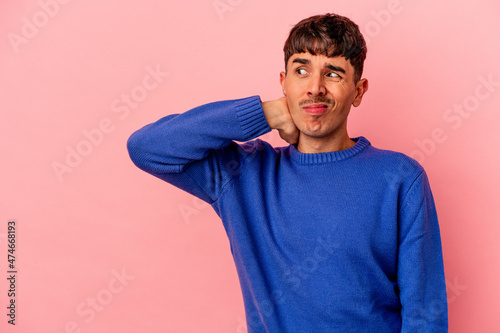Young mixed race man isolated on pink background touching back of head, thinking and making a choice.