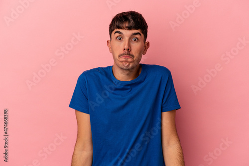 Young mixed race man isolated on pink background shrugs shoulders and open eyes confused.