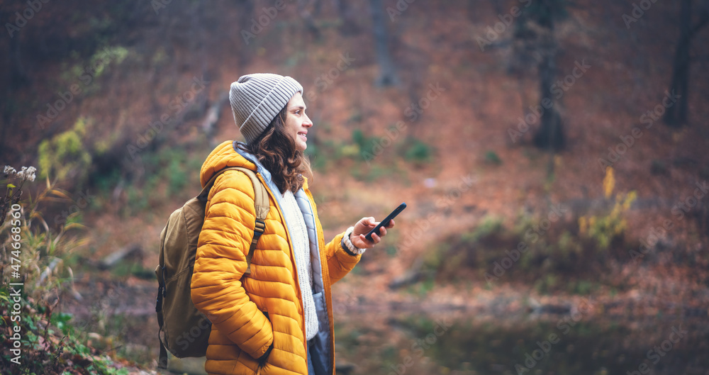 Naklejka premium Young woman traveler in yellow jacket and hat with backpack with mobile phone smartphone in hands