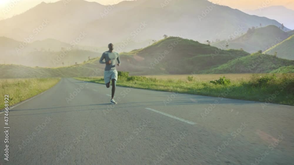 Young African American Man Running at Sunset Background. Mountain View. Athlete Running Fast Down the Road. Sport Workout Outdoor. Beautiful Sunset. Young African American Man Running at Sunset Background. Mountain View. Athlete Running Fast Down the Road. Sport Workout Outdoor. Beautiful Sunset.