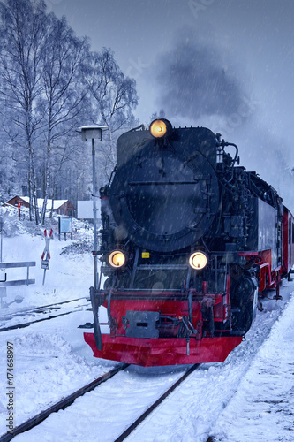 Black steam locomotive with yellow headlights runs over snowy tracks in heavy snowfall