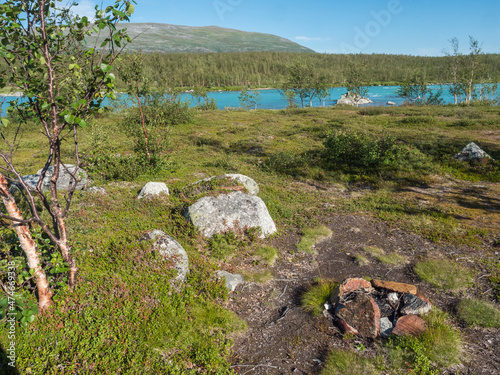 Beatiful camping spot in northern landscape in Swedish Lapland with turquoise blue Vuojatadno river, birch tree forest and green mountains at Padjelantaleden hiking trail. Summer sunny day, blue sky photo