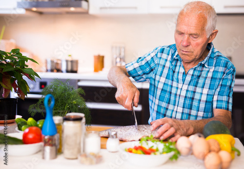 elderly man preparing fish at home in the kitchen