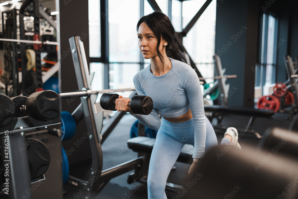 Woman shakes biceps doing exercises with dumbbells Woman shakes biceps doing exercises with dumbbells