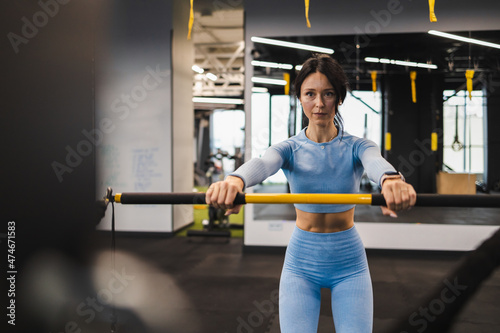 Fitness woman in blue sportswear is training with a trx rip trainer in the gym