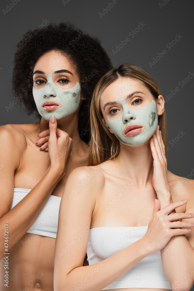 pretty multiethnic women in clay masks looking at camera while posing isolated on grey pretty multiethnic women in clay masks looking at camera while posing isolated on grey