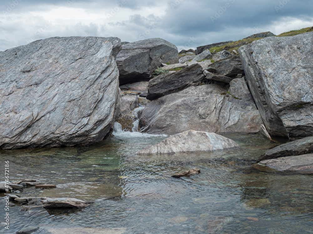 Water runs over the top of big grey stone boulders at water stream at arctic northern landscape in Swedish Lapland Water runs over the top of big grey stone boulders at water stream at arctic northern landscape in Swedish Lapland