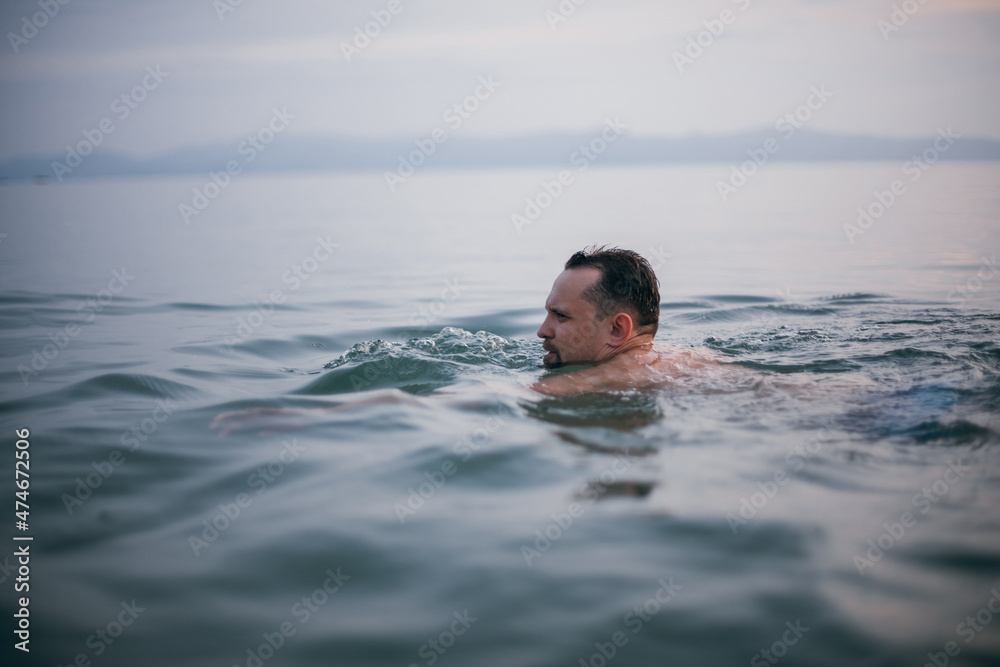 A man swims in the ocean at sunset