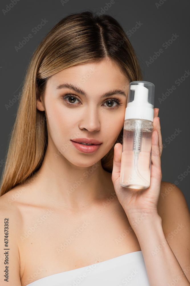 young woman with perfect skin showing bottle of face foam isolated on grey young woman with perfect skin showing bottle of face foam isolated on grey