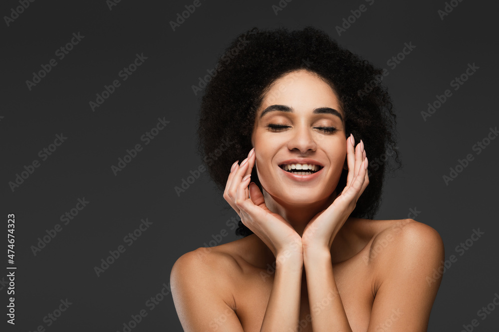 happy african american woman with closed eyes touching perfect skin on face isolated on grey happy african american woman with closed eyes touching perfect skin on face isolated on grey